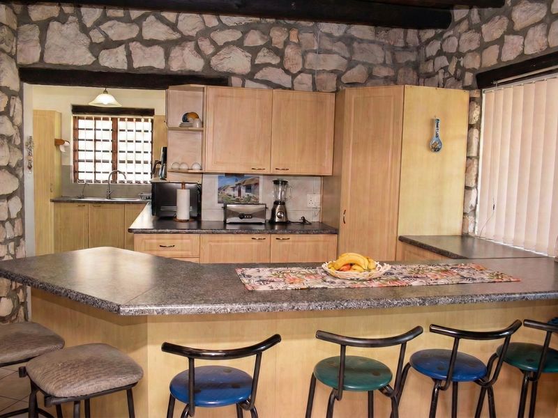 Rustic kitchen featuring stone wall cladding, exposed timber beams, laminate cabinetry, and a breakfast bar with integrated prep area.