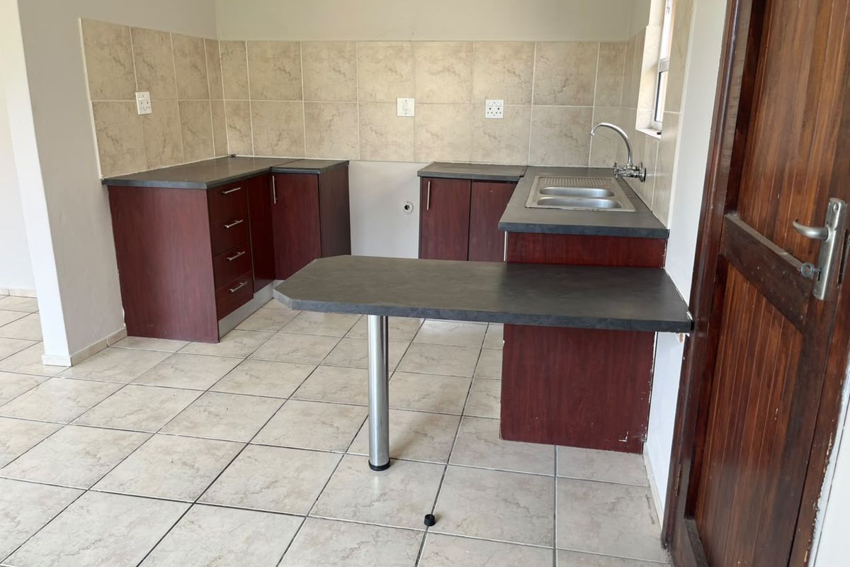 A functional, empty kitchen featuring laminate cabinetry, a breakfast bar, and tiled finishes, ready for personalization or appliance installation.