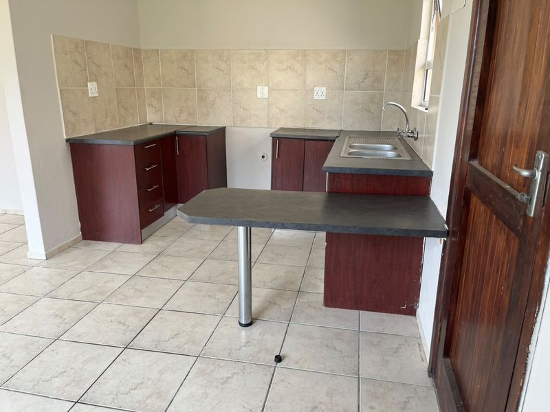 A functional, empty kitchen featuring laminate cabinetry, a breakfast bar, and tiled finishes, ready for personalization or appliance installation.