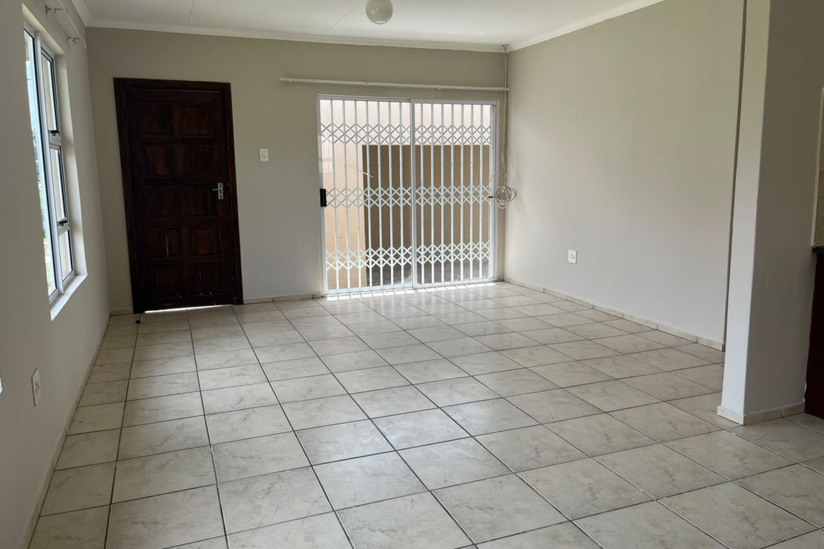 A spacious, empty living area featuring neutral tiled flooring, a solid timber door, and a sliding glass door with a security gate leading outside.