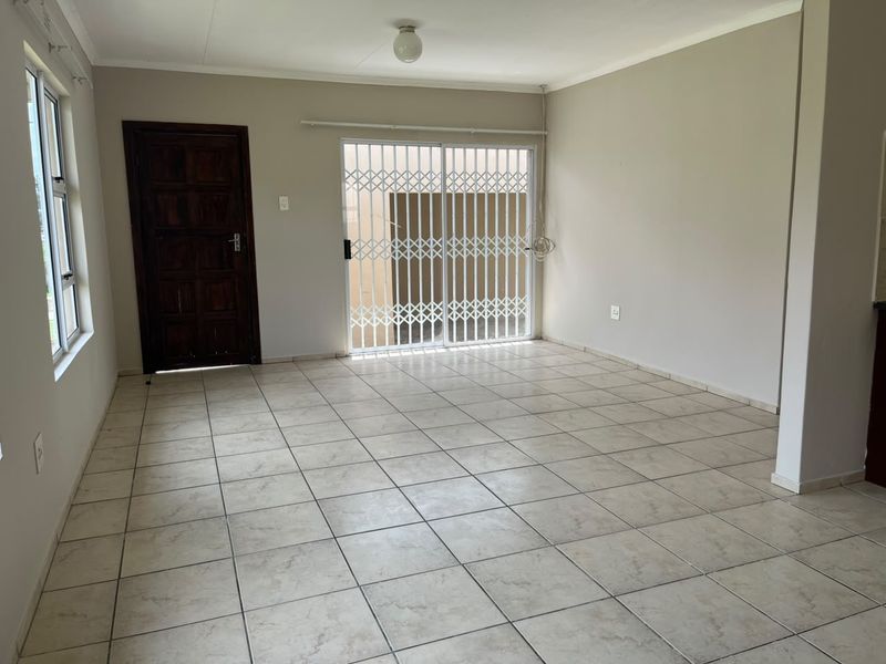 A spacious, empty living area featuring neutral tiled flooring, a solid timber door, and a sliding glass door with a security gate leading outside.
