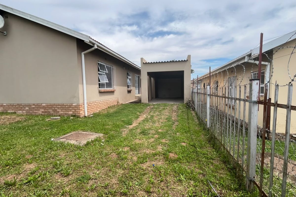 Rear exterior view showing a detached carport, brick and plaster wall finishes, and metal perimeter fencing with security razor wire.