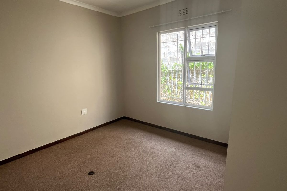 An empty bedroom featuring neutral walls, carpet flooring, and a window fitted with security bars.