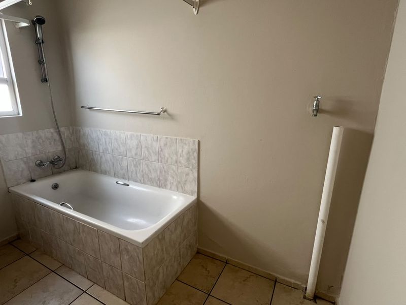 A functional bathroom featuring a built-in bathtub with shower mixer, tiled splashback, and tiled flooring, currently requiring minor finishing work to the wall and plumbing.