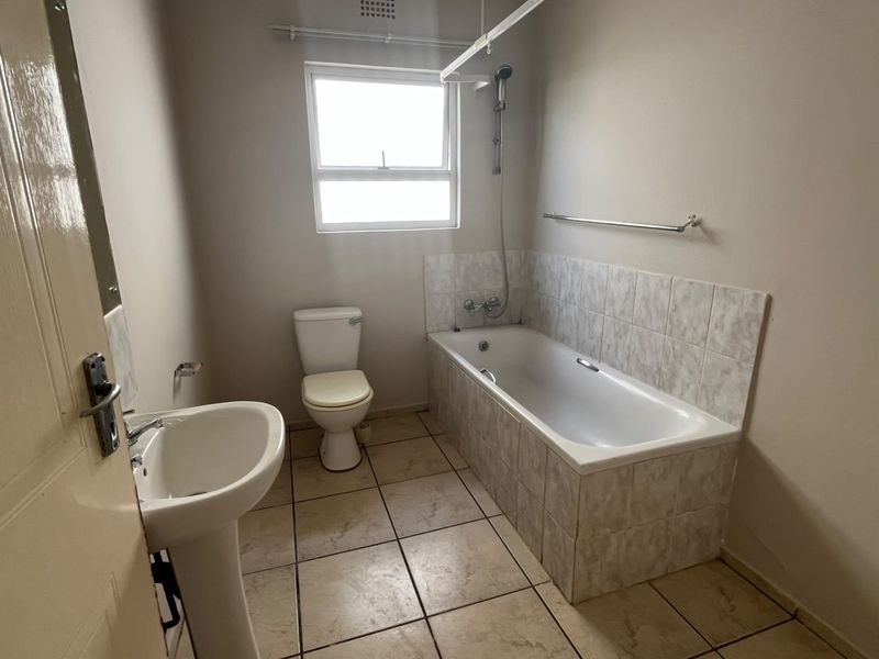 A functional bathroom featuring a pedestal basin, toilet, and a tiled bathtub with a shower mixer, offering a clean and neutral space.