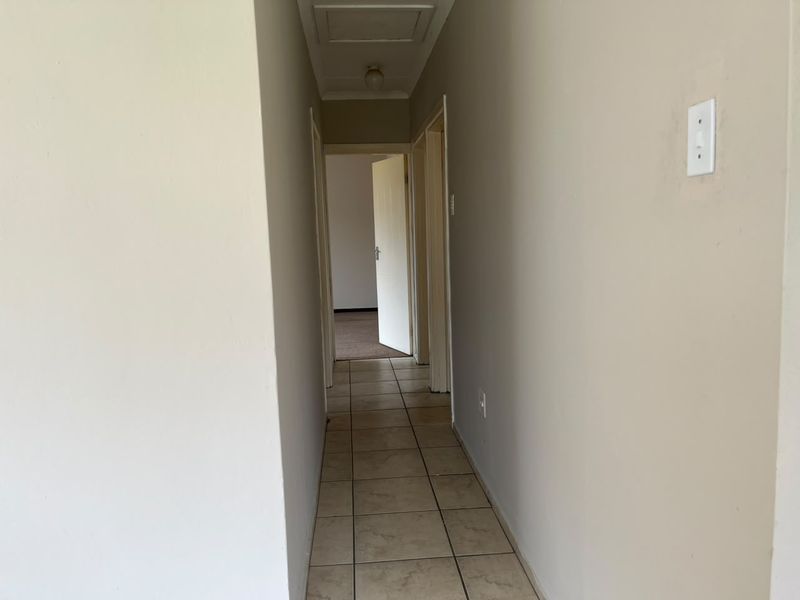 A simple, neutral-toned hallway featuring tiled flooring and access to adjacent rooms, providing a clean and functional transition space within the home.
