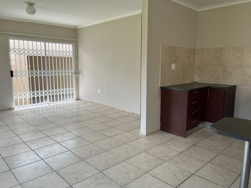An open-plan living and kitchen area featuring tiled flooring, built-in cabinetry with a tiled backsplash, and a sliding door with a security gate.