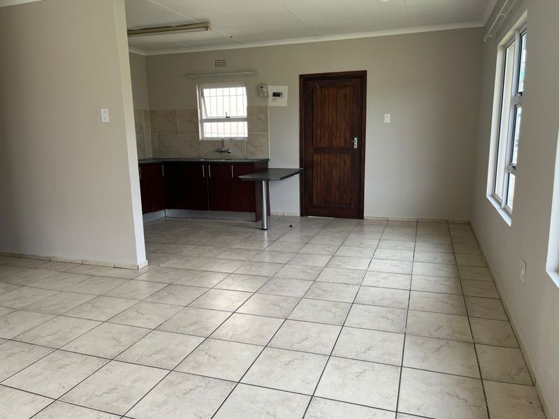 An open-plan living and kitchen area featuring tiled flooring, built-in cabinetry with a breakfast counter, and a secure timber entrance door.