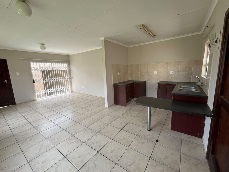 An open-plan living and kitchen area featuring tiled flooring, built-in cabinetry with laminate countertops, and a security gate leading to the exterior.