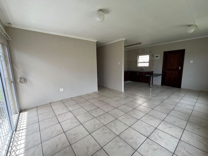 Open-plan living area featuring tiled flooring and a compact kitchen space with built-in cabinetry and sink.