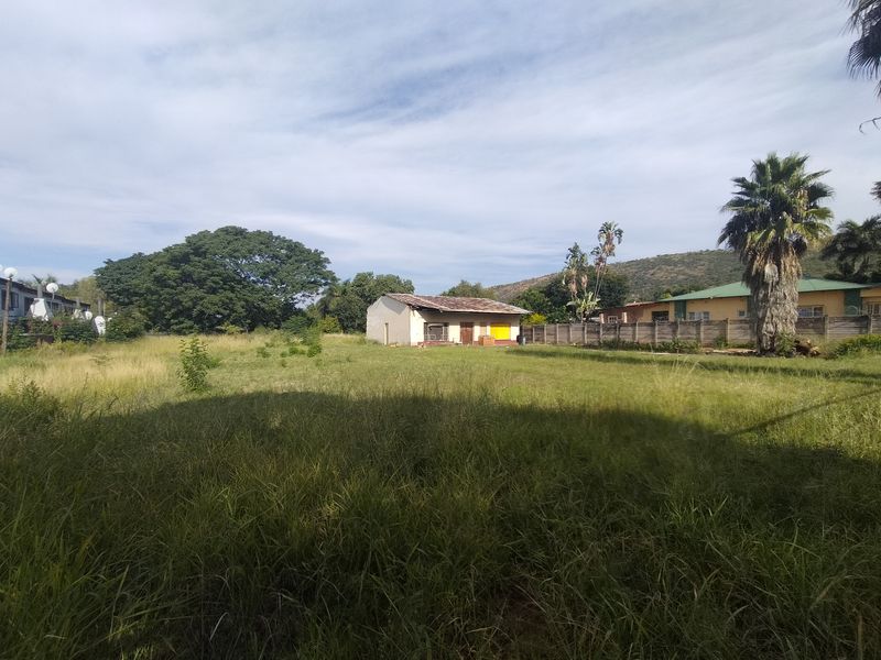 A large, overgrown vacant residential plot featuring a small, weathered structure and perimeter walling, offering significant potential for development.