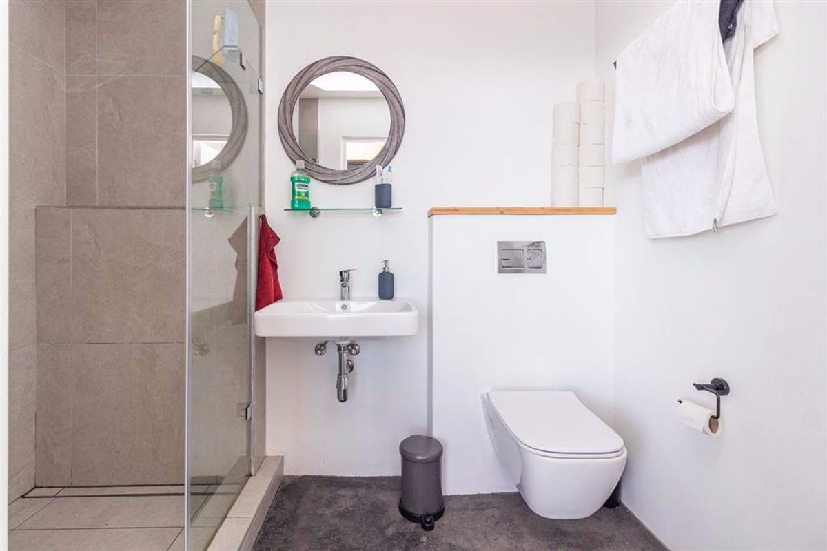 Modern bathroom featuring a wall-mounted toilet with concealed cistern, a wall-mounted basin, and a glass-enclosed shower with neutral tiling.