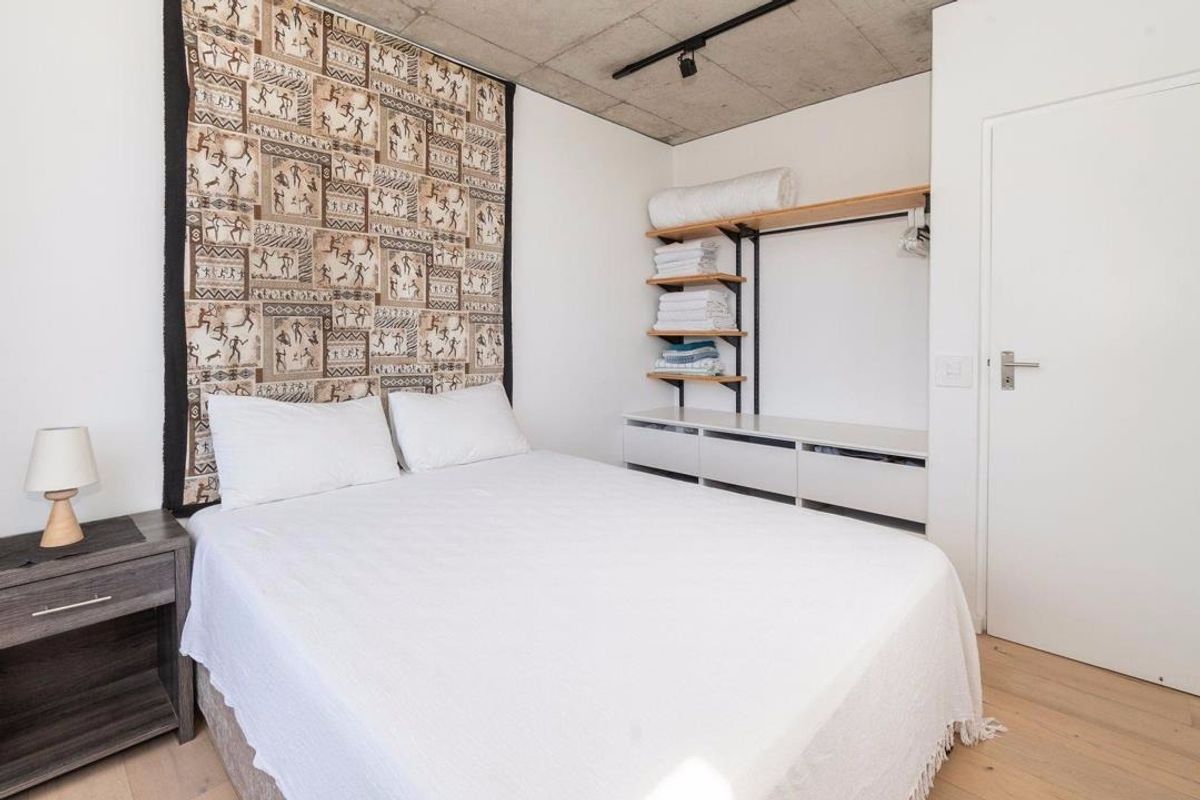Modern bedroom featuring an exposed concrete ceiling, timber flooring, and practical built-in open shelving with integrated storage.