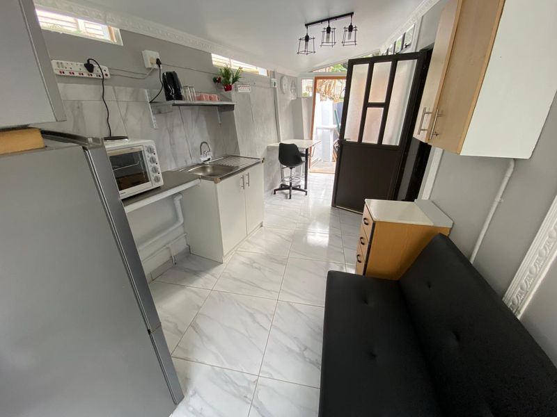 Compact kitchen area featuring marble-look floor tiles, built-in cabinetry, stainless steel sink, and direct access to an outdoor space.