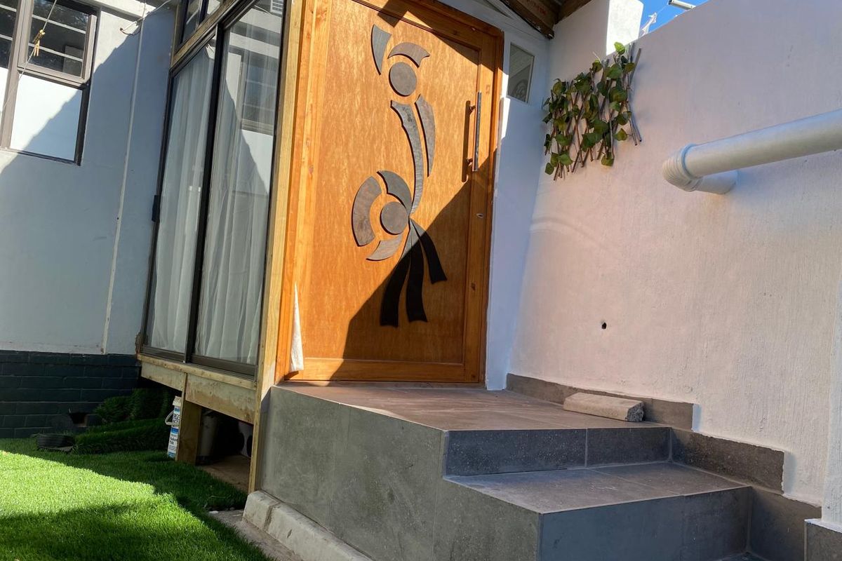 Rear exterior view featuring a decorative timber entrance door, tiled steps, and an adjacent aluminium sliding door leading into the home.