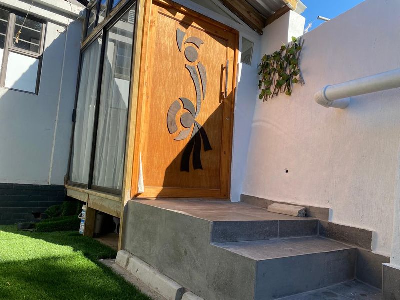 Rear exterior view featuring a decorative timber entrance door, tiled steps, and an adjacent aluminium sliding door leading into the home.