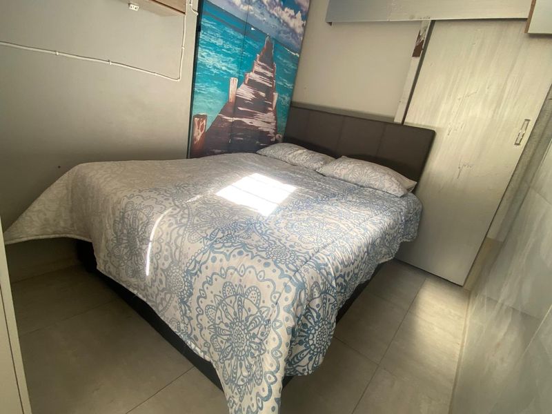 A compact bedroom featuring tiled flooring and a built-in wardrobe, offering a functional space that could benefit from cosmetic updates.