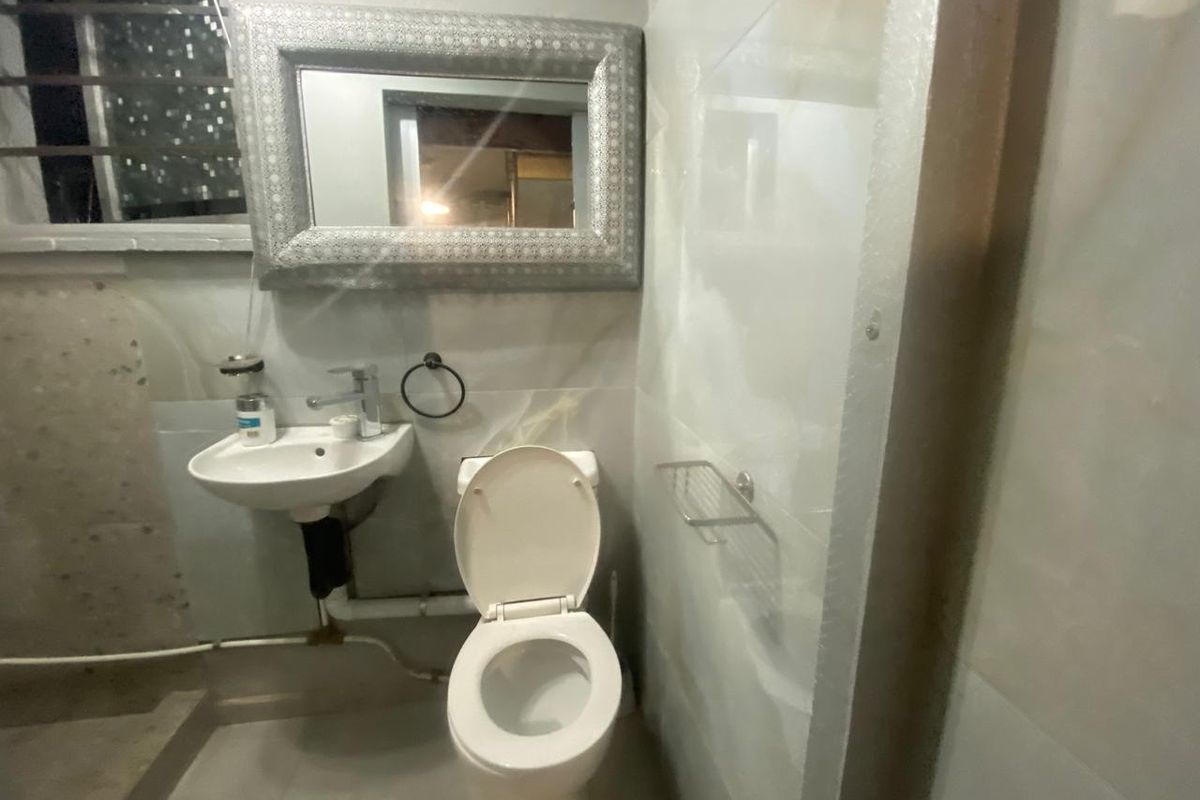 A compact bathroom featuring a wall-mounted basin and toilet with tiled surfaces, requiring cosmetic updates to improve the finish and hide exposed plumbing.