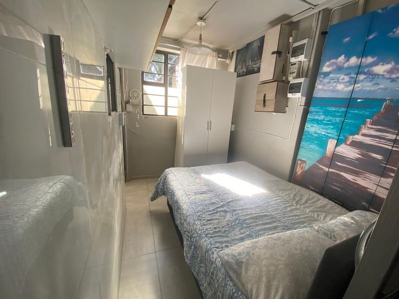 A compact bedroom featuring tiled flooring, a window, and wall-mounted electrical distribution components.