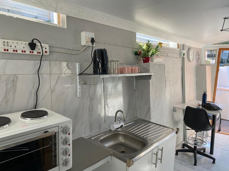Compact kitchen area featuring marble-look splashback tiles, stainless steel sink, and built-in cabinetry with crown molding detail.