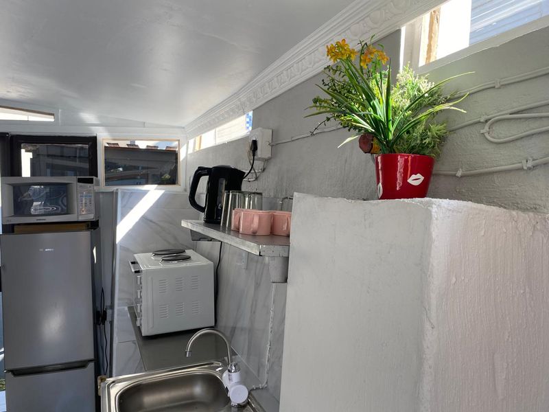 Compact kitchen area featuring a stainless steel sink, built-in microwave, and basic shelving with exposed electrical conduit and textured wall finishes.