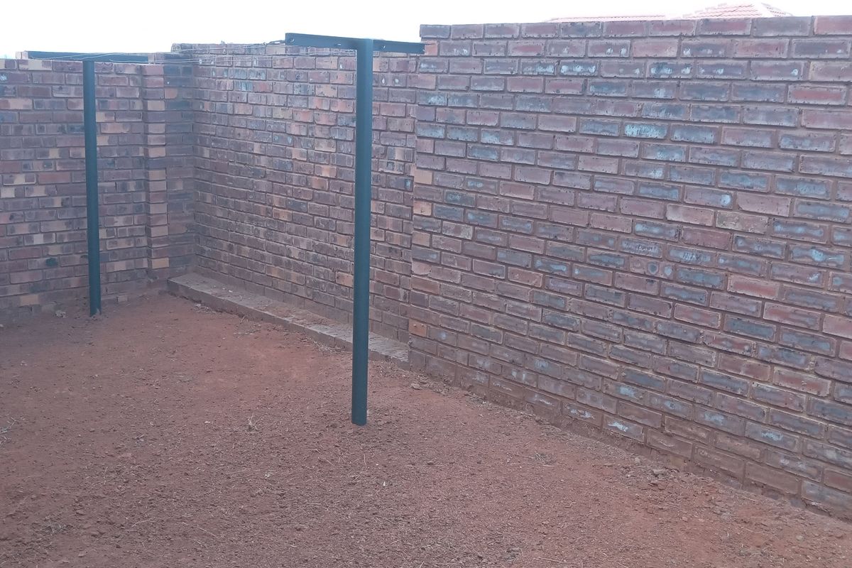 An outdoor utility or courtyard area featuring exposed brick boundary walls and metal support posts, currently awaiting landscaping or paving.