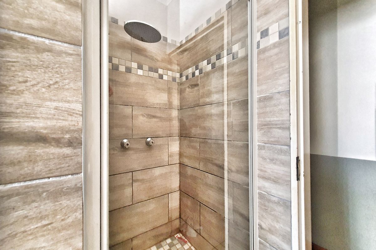 A walk-in shower featuring wood-look ceramic wall tiles, a glass enclosure, and a modern rainfall shower head.