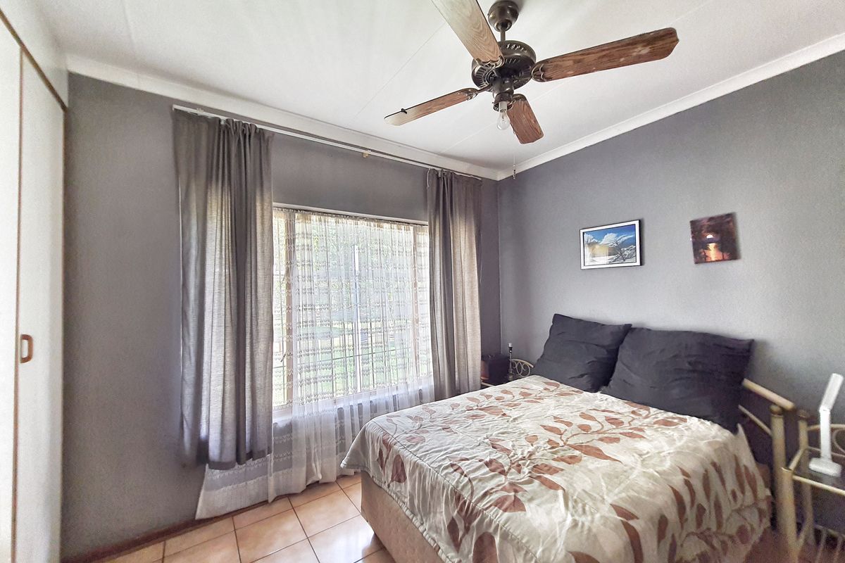 A bedroom featuring tiled flooring, a ceiling fan, and a built-in wardrobe, offering a functional and comfortable living space.