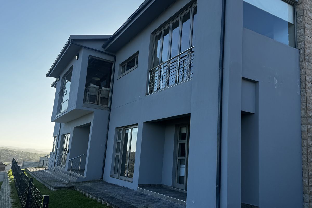 Rear elevation of a modern multi-story house featuring grey rendered walls, stone cladding accents, aluminium windows, and stainless steel balustrades.