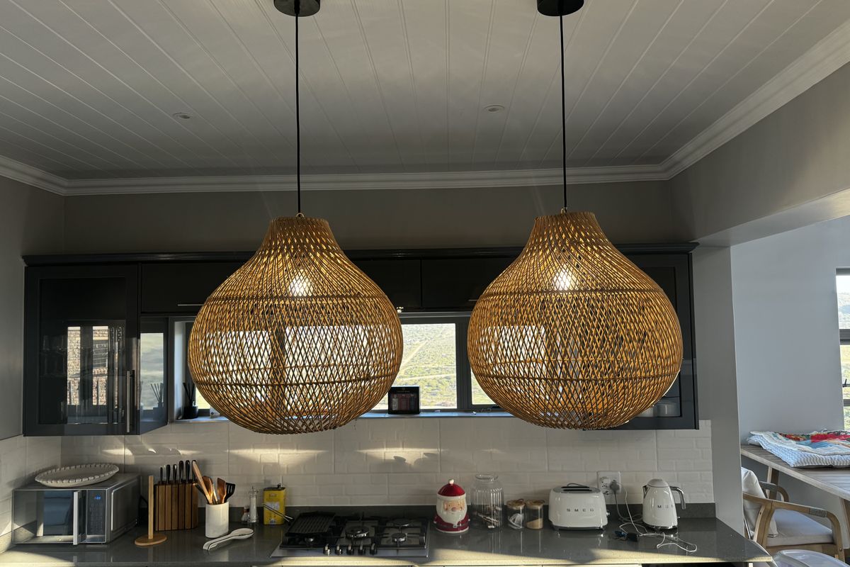Modern kitchen featuring dark cabinetry, stone countertops, subway tile backsplash, and stylish woven pendant lights over the cooking area.