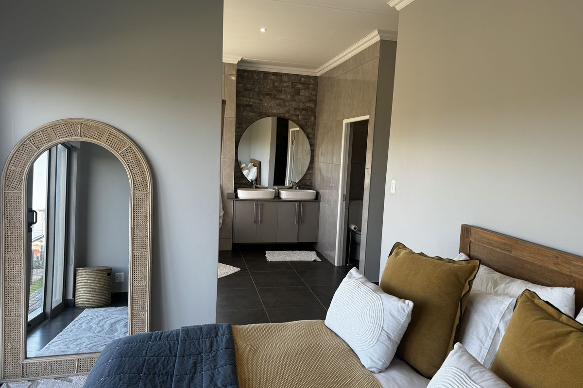 A well-maintained bedroom featuring an open-plan en-suite bathroom with a double vanity, stone feature wall, and modern tiled flooring.