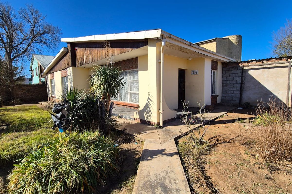 Front elevation of a single-story house featuring a covered porch, concrete walkway, and established garden area.