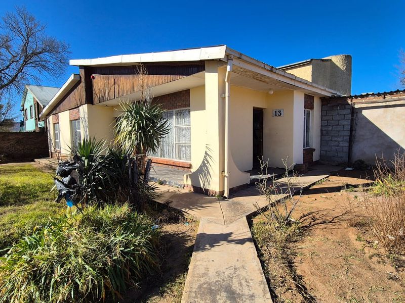 Front elevation of a single-story house featuring a covered porch, concrete walkway, and established garden area.