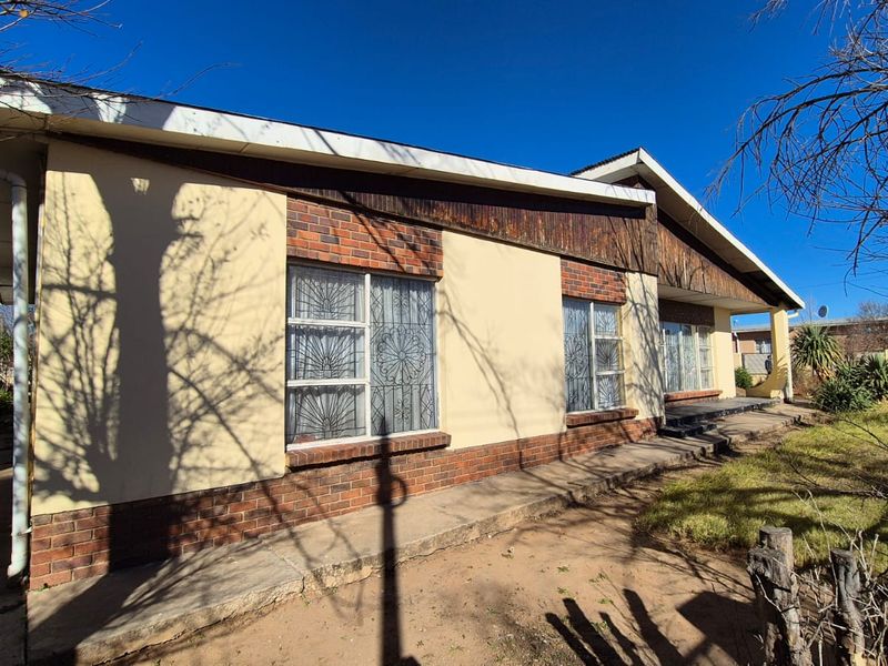 Front elevation of a single-story house featuring brick and plaster finishes, security bars on windows, and a concrete walkway.