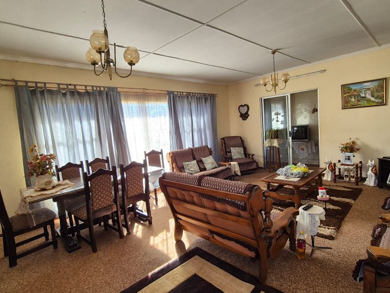 Spacious open-plan living and dining area featuring carpeted flooring, sliding glass doors, and traditional ceiling tiles, offering a versatile layout for family living.