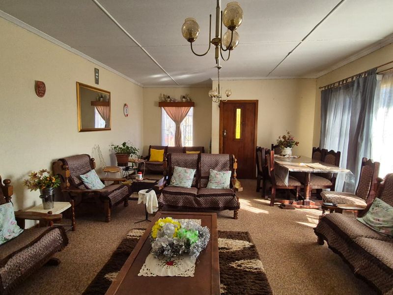 Spacious open-plan living and dining area featuring traditional ceiling finishes, carpeted flooring, and natural light through window security bars.
