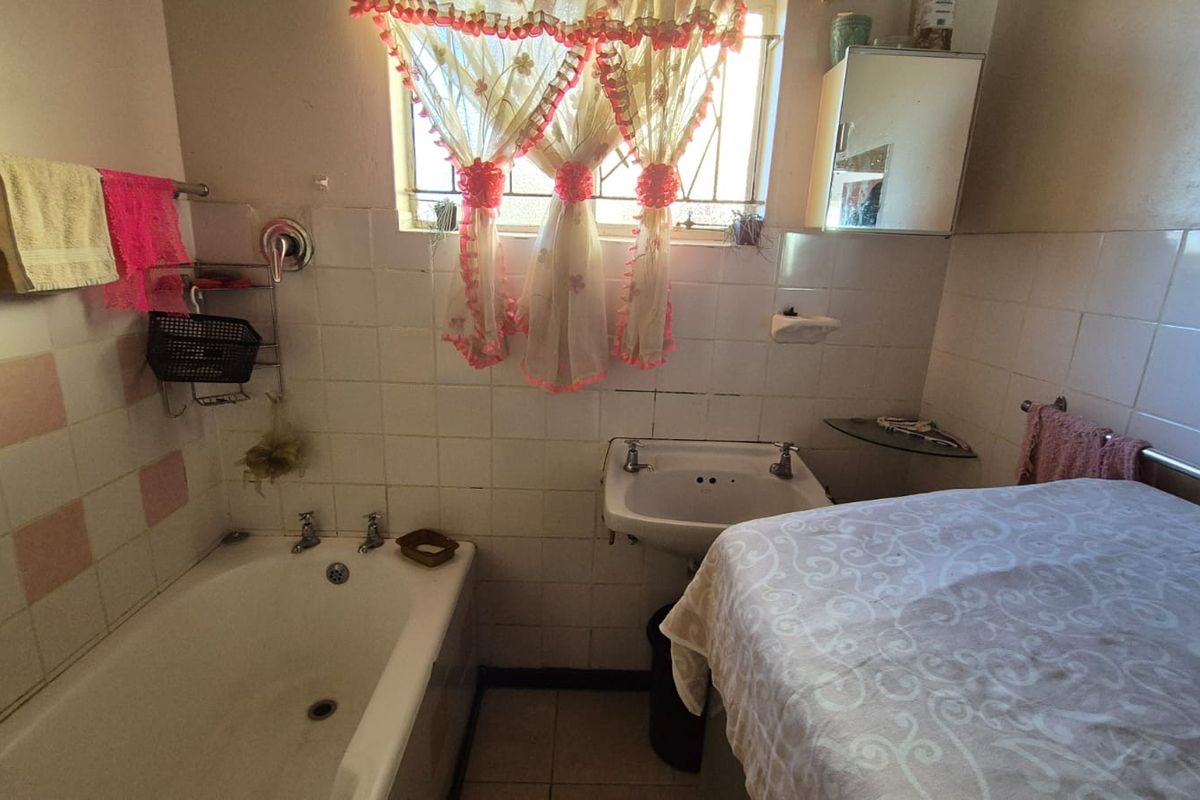 A dated bathroom featuring a standard bathtub, pedestal basin, and wall tiling, requiring modernization to improve its aesthetic and functionality.