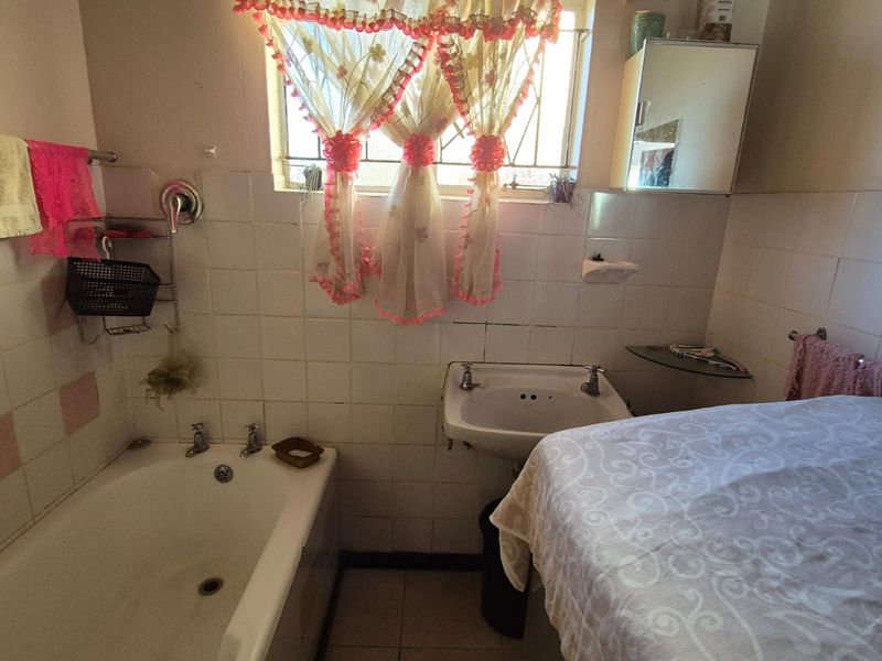 A dated bathroom featuring a standard bathtub, pedestal basin, and wall tiling, requiring modernization to improve its aesthetic and functionality.