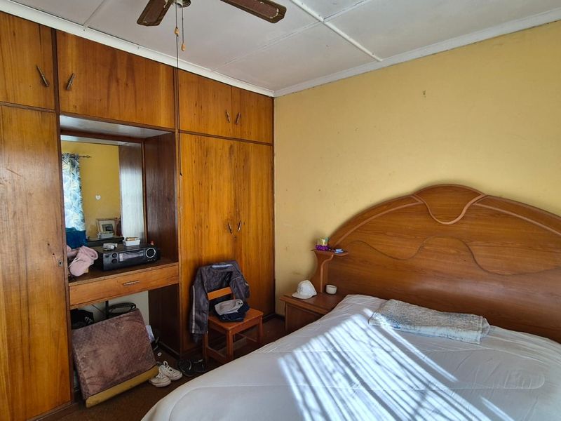 A bedroom featuring extensive built-in wooden cabinetry and a ceiling fan, requiring cosmetic updates to the wall finishes and ceiling.