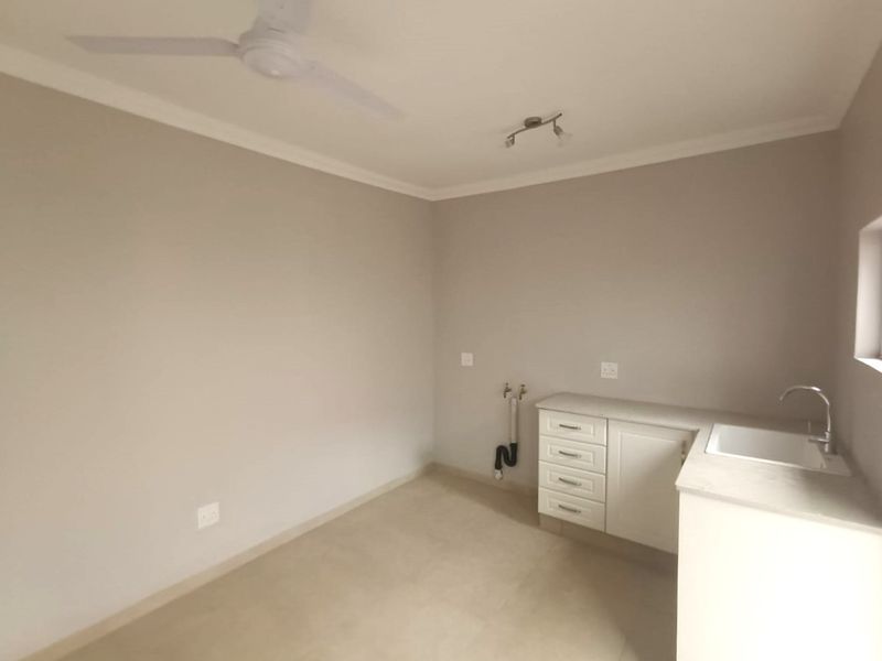 A clean, empty laundry room featuring built-in cabinetry, a sink, and plumbing connections for appliances.