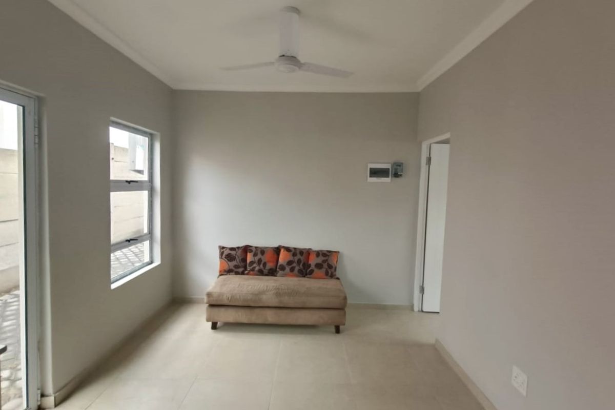 A bright living area featuring neutral tiled flooring, a ceiling fan, and clean wall finishes, providing a versatile space for relaxation.