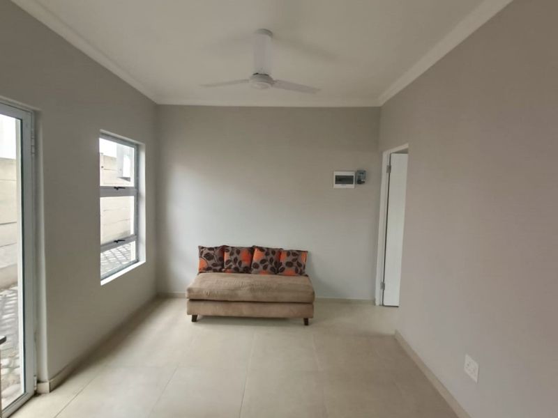 A bright living area featuring neutral tiled flooring, a ceiling fan, and clean wall finishes, providing a versatile space for relaxation.