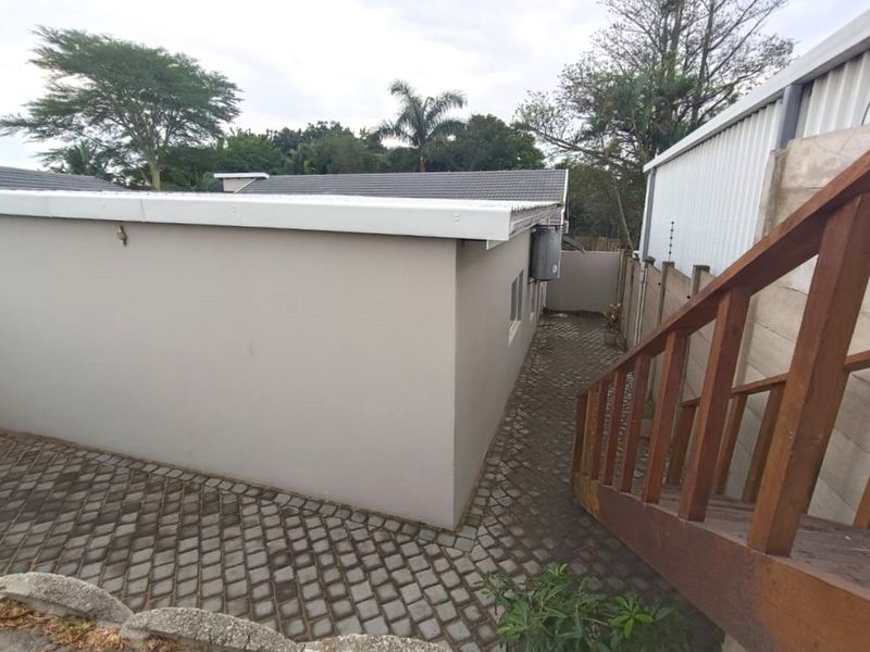 Rear exterior view of the property featuring a paved walkway, timber staircase, and secure boundary wall with electric fencing.