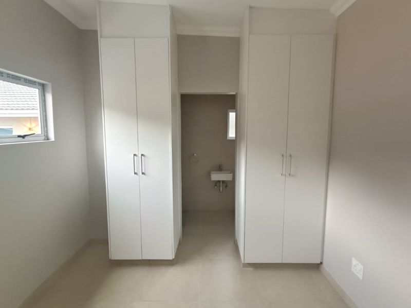 A clean, modern bedroom featuring built-in cupboards and an adjoining en-suite area with a wall-mounted basin.