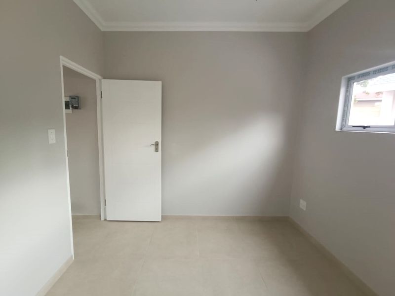 A clean, neutral-toned bedroom featuring tiled flooring, coved ceilings, and an aluminium window, offering a blank canvas for interior design.