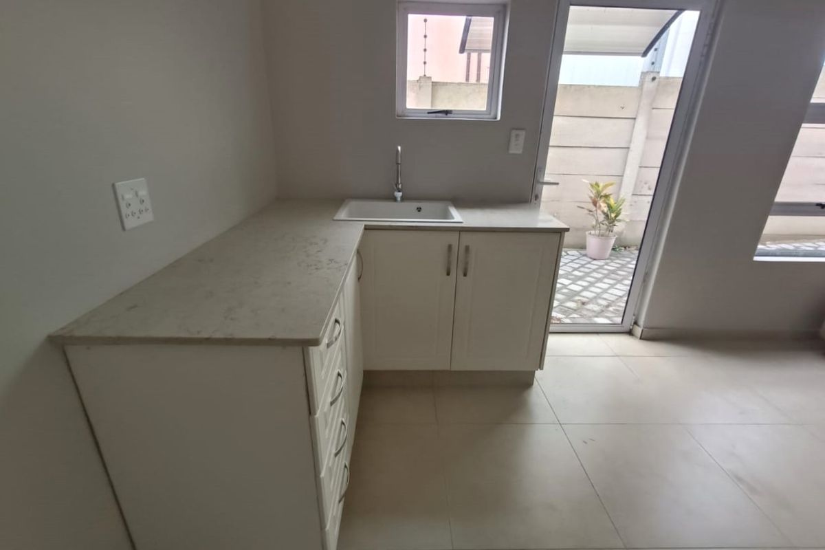 A clean, modern kitchen area featuring white cabinetry, stone countertops, an undermount sink, and direct access to an outdoor patio area.