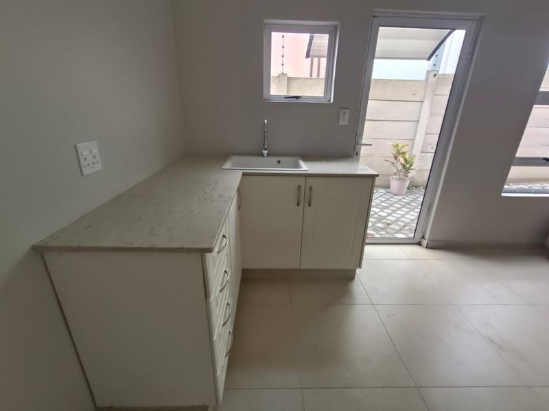 A clean, modern kitchen area featuring white cabinetry, stone countertops, an undermount sink, and direct access to an outdoor patio area.
