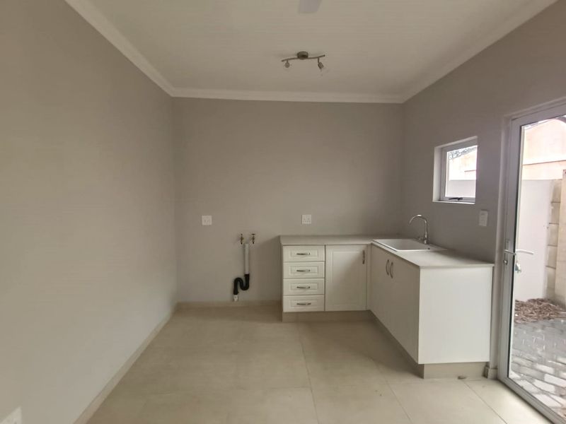 A clean and functional laundry room featuring built-in cabinetry, a sink, and plumbing connections for appliances, with direct access to an outdoor area.