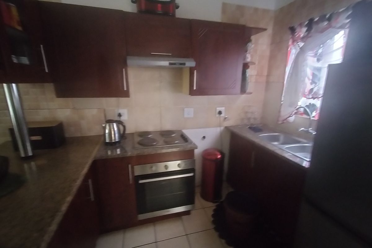A functional kitchen featuring dark wood cabinetry, granite countertops, a built-in oven with electric hob, and a double sink with tiled backsplash.