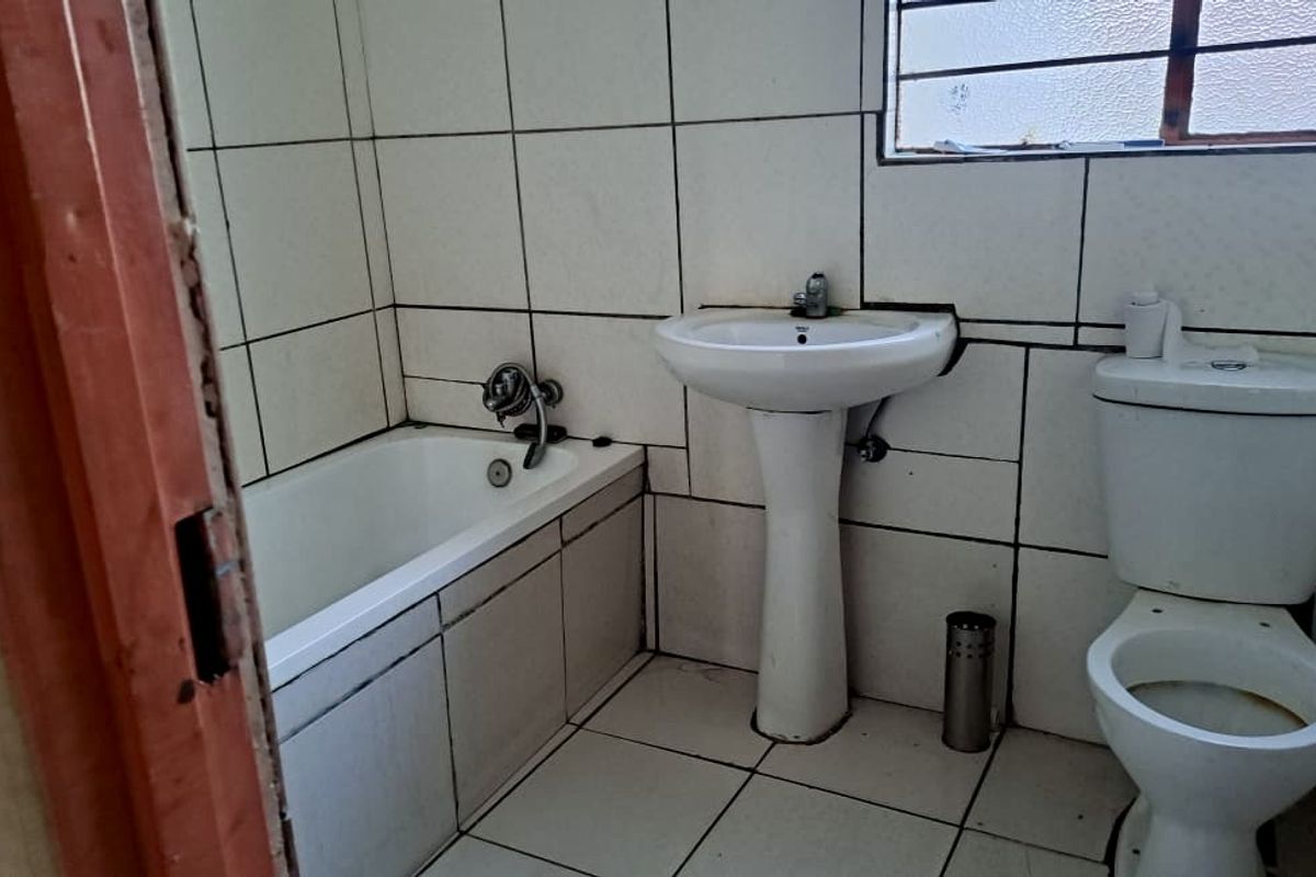 A dated bathroom featuring a standard bathtub, pedestal basin, and toilet with original wall and floor tiling.